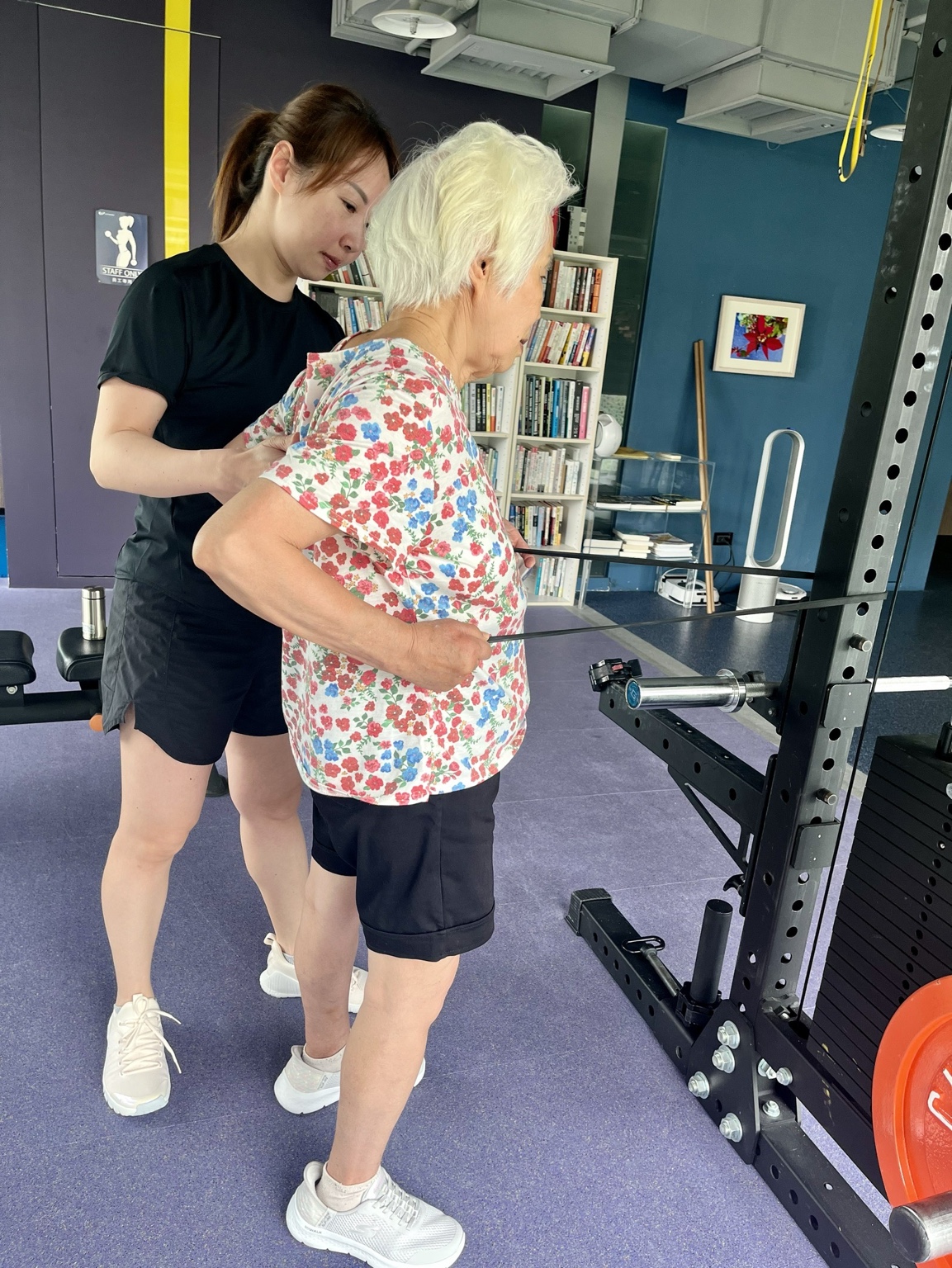 Claire 教練在旁觀察並引導 Joanne 周阿嬤進行彈力帶划船